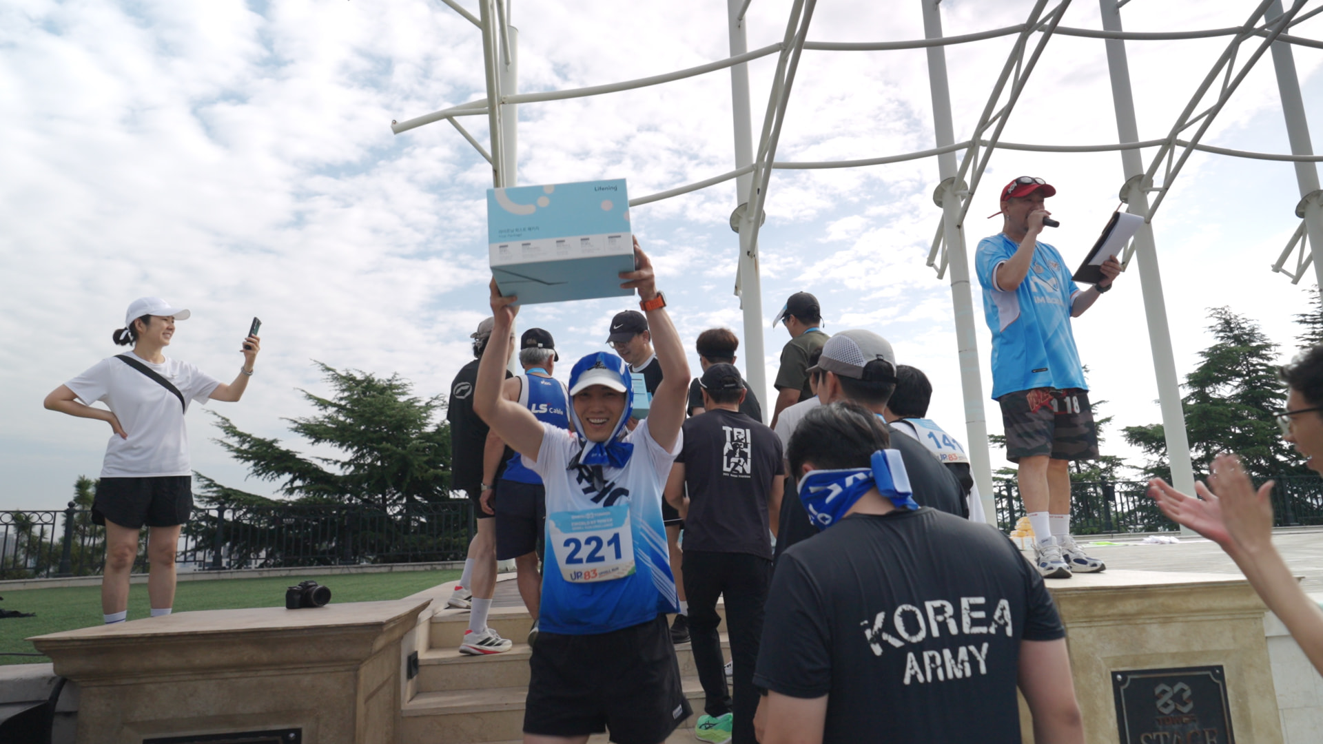 스테이지에서 럭키드로우 경품 상자를 들어 올리는 참가자와 진행 MC