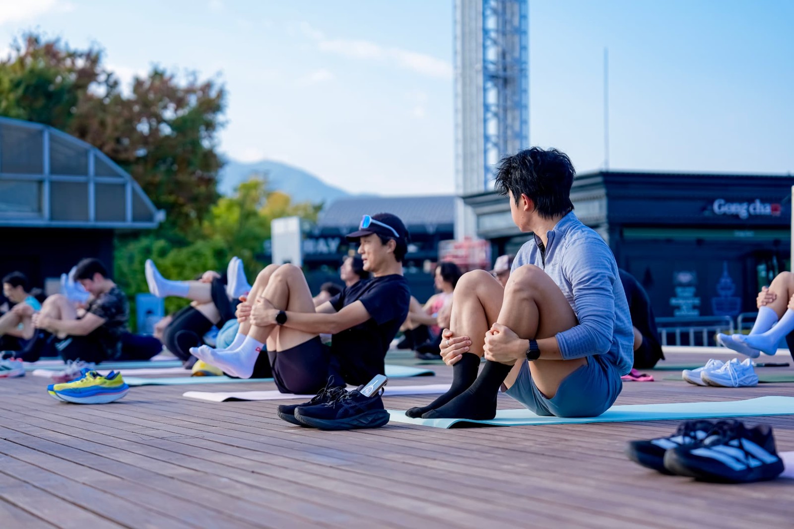 야외 요가 매트에 앉아 무릎을 안고 스트레칭하는 참가자들